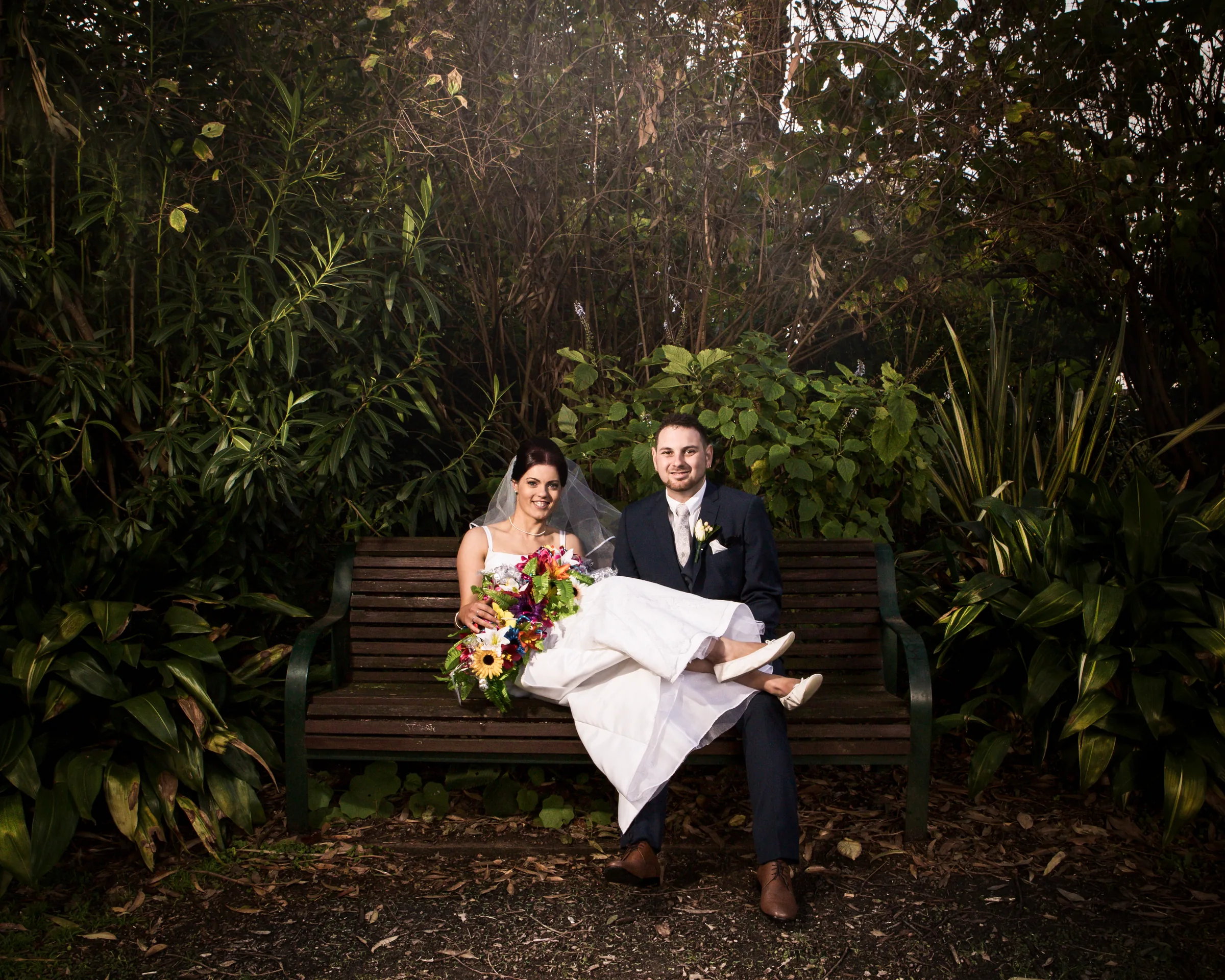 A newly married couple sit close together in a sunlit garden, photographed by Royale Photography.